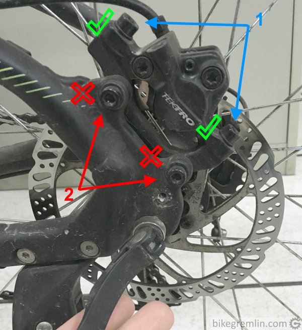 Loosening brake caliper bolts (1), NOT brake adaptor bolts (2).